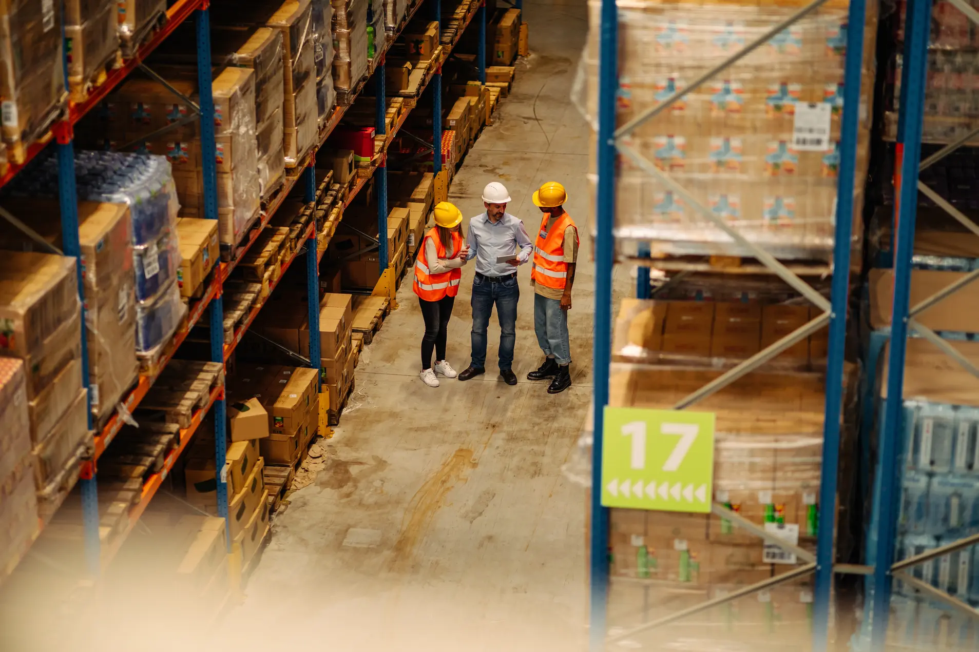 Warehouse interior with high shelves stacked with pallets and boxes, and a worker operating a yellow forklift to organize inventory.