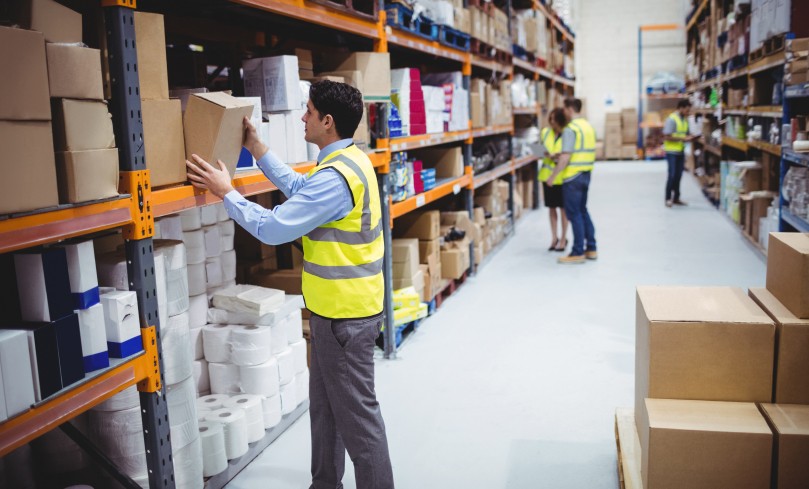 Warehouse workers in high-visibility vests organizing boxes and inventory on shelves, demonstrating efficient stock management in a busy warehouse environment.